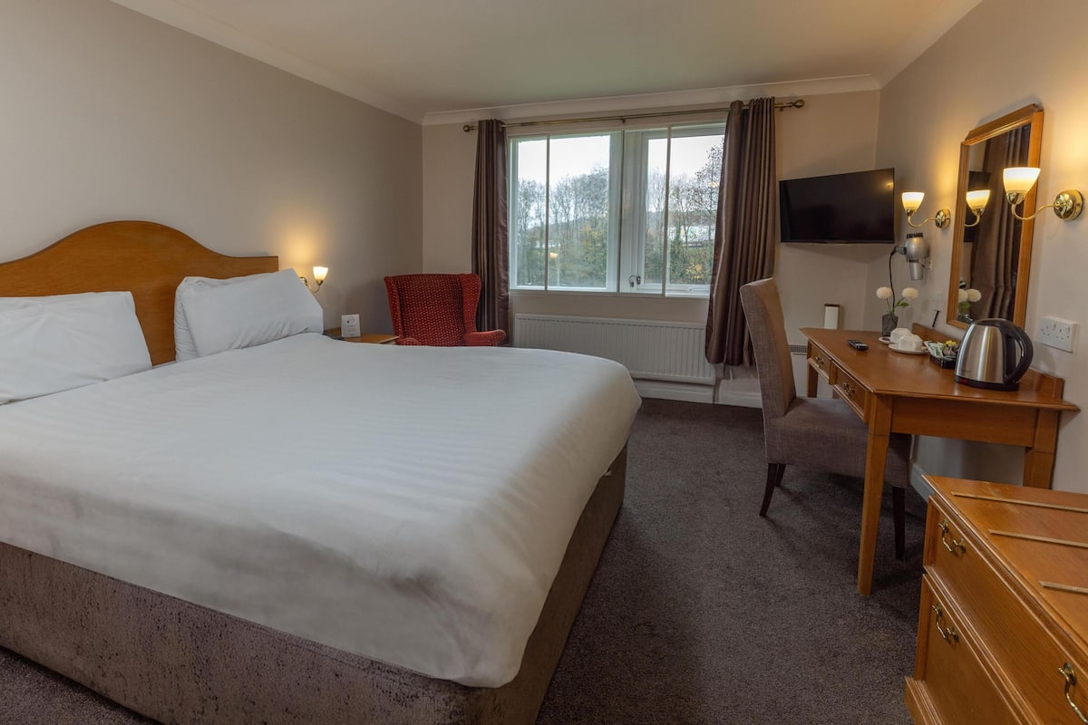 A hotel room with a large bed, a desk with a chair, a television, and a window with curtains.
