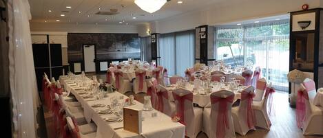 A banquet hall with long tables, white tablecloths, and chairs with pink sashes.