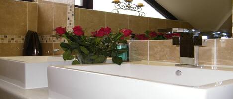 A bathroom with two white sinks, a vase of red roses, and a mirror above the sinks.