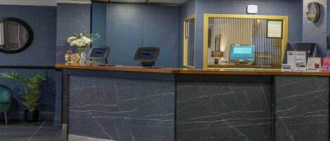 A reception desk with a marble front, two monitors, a vase with flowers, and a clock on the wall.