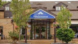 Un bâtiment avec une pancarte « Bienvenue », une façade en pierre et un petit jardin agrémenté de plantes en pot.