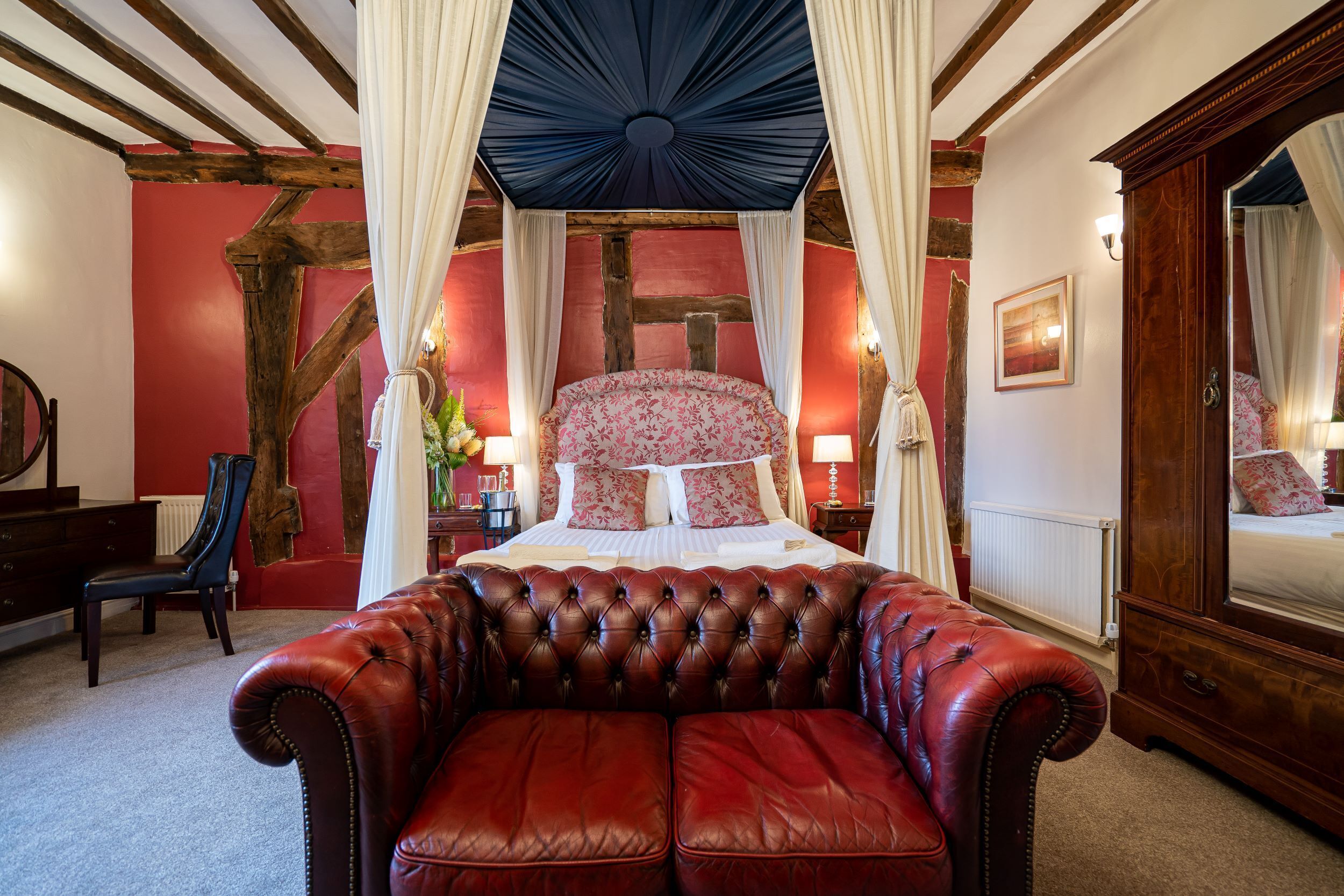 Een slaapkamer met een hemelbed, een rode leren bank en een houten garderobe.