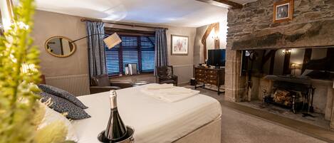 A cozy bedroom with a large bed, a fireplace, a stone wall, and a mirror.