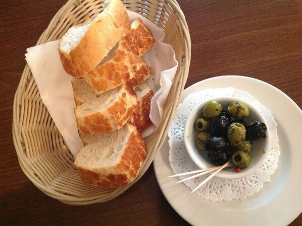 A basket of sliced bread and a small bowl of olives on a table.