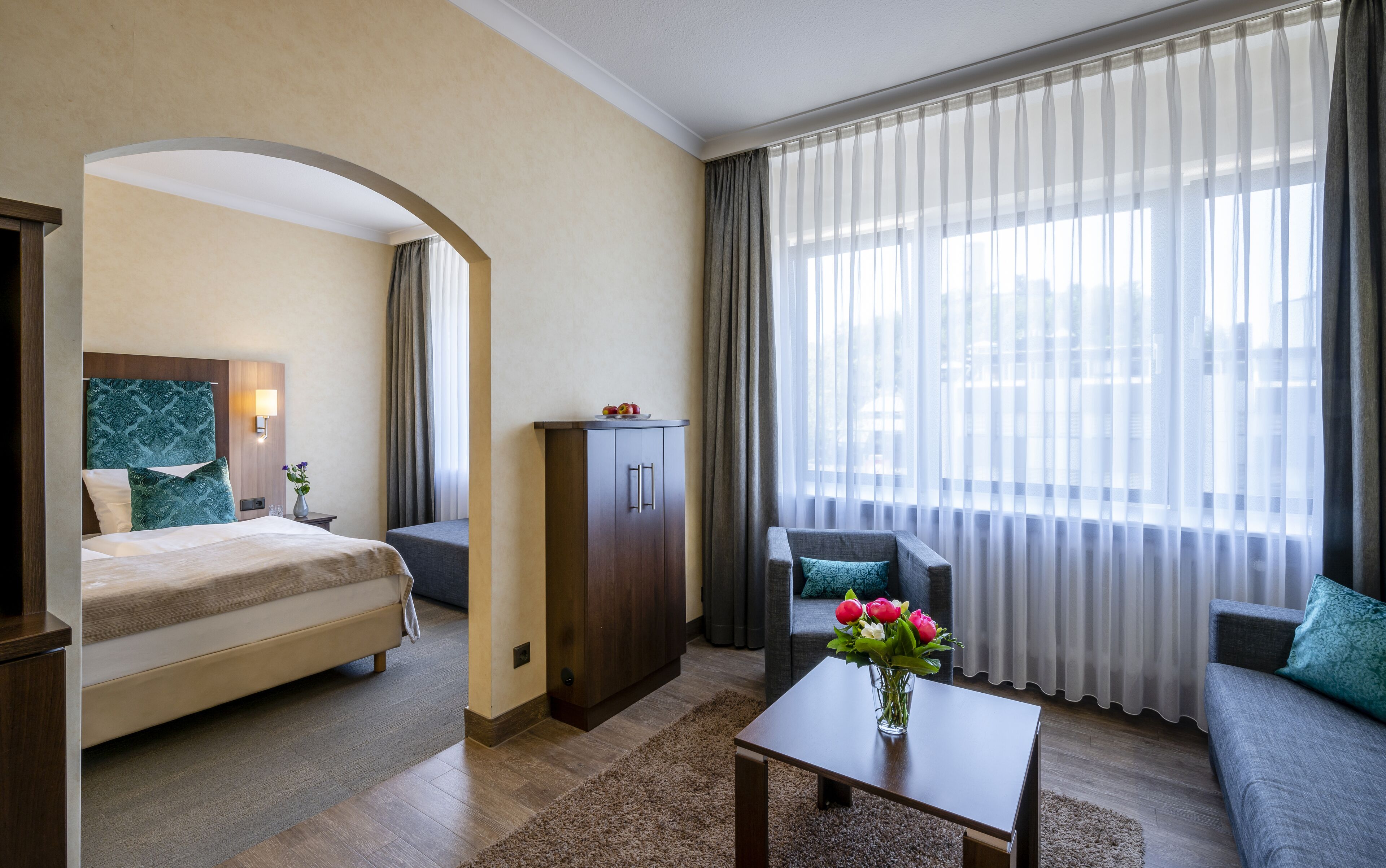Una habitación de hotel con cama, escritorio, sofá y un gran ventanal con cortinas.