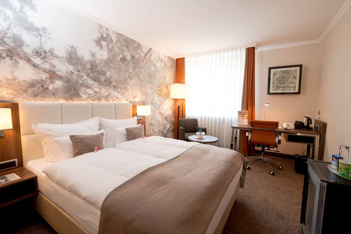 Une chambre d’hôtel avec un grand lit, un bureau, une chaise, une lampe et un tableau au mur.
