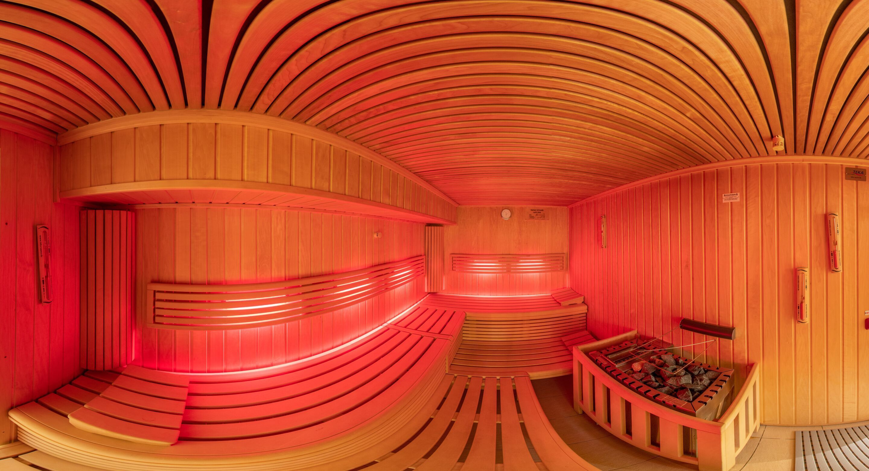 A sauna with curved wooden walls and benches, a wooden bench with a fire, and a small clock on the wall.