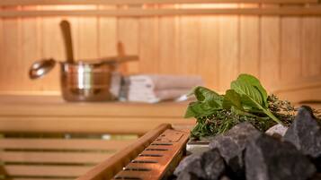 A sauna with wooden benches, a metal container, and fresh herbs.