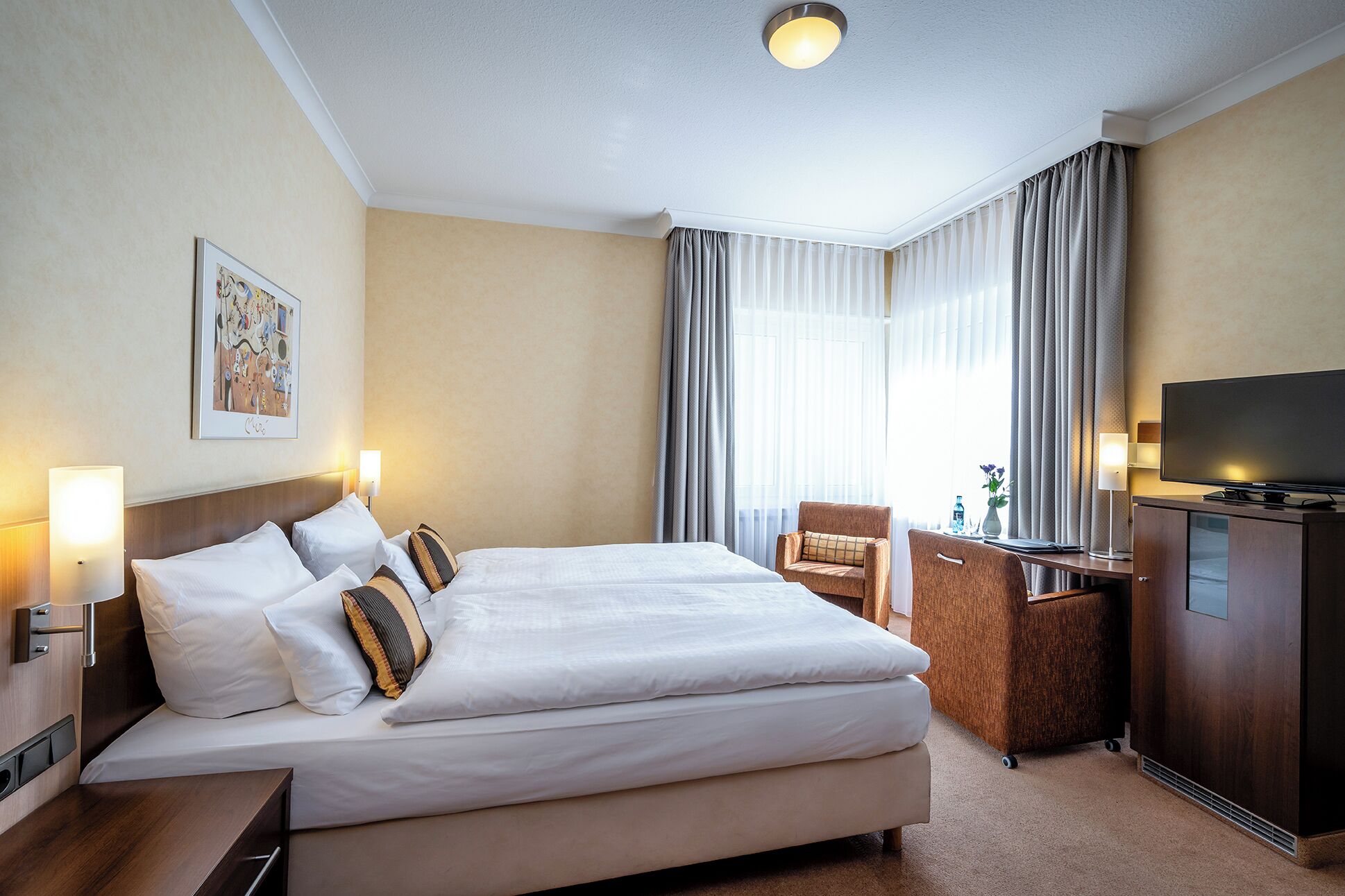 Een hotelkamer met een groot bed, een bureau, een stoel, een televisie en een schilderij aan de muur.