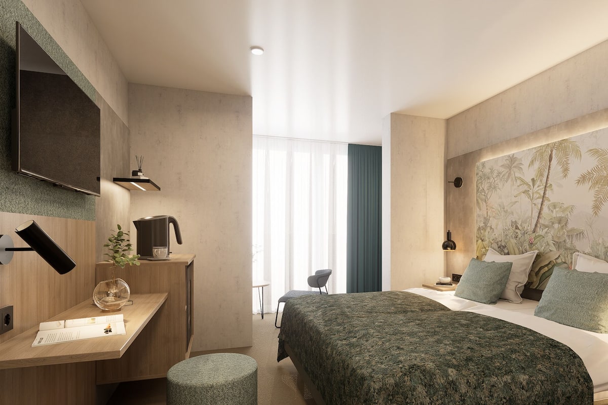 Une chambre d’hôtel moderne équipée d’un lit, d’un bureau, d’un téléviseur fixé au mur et d’une grande fenêtre avec des rideaux légers.