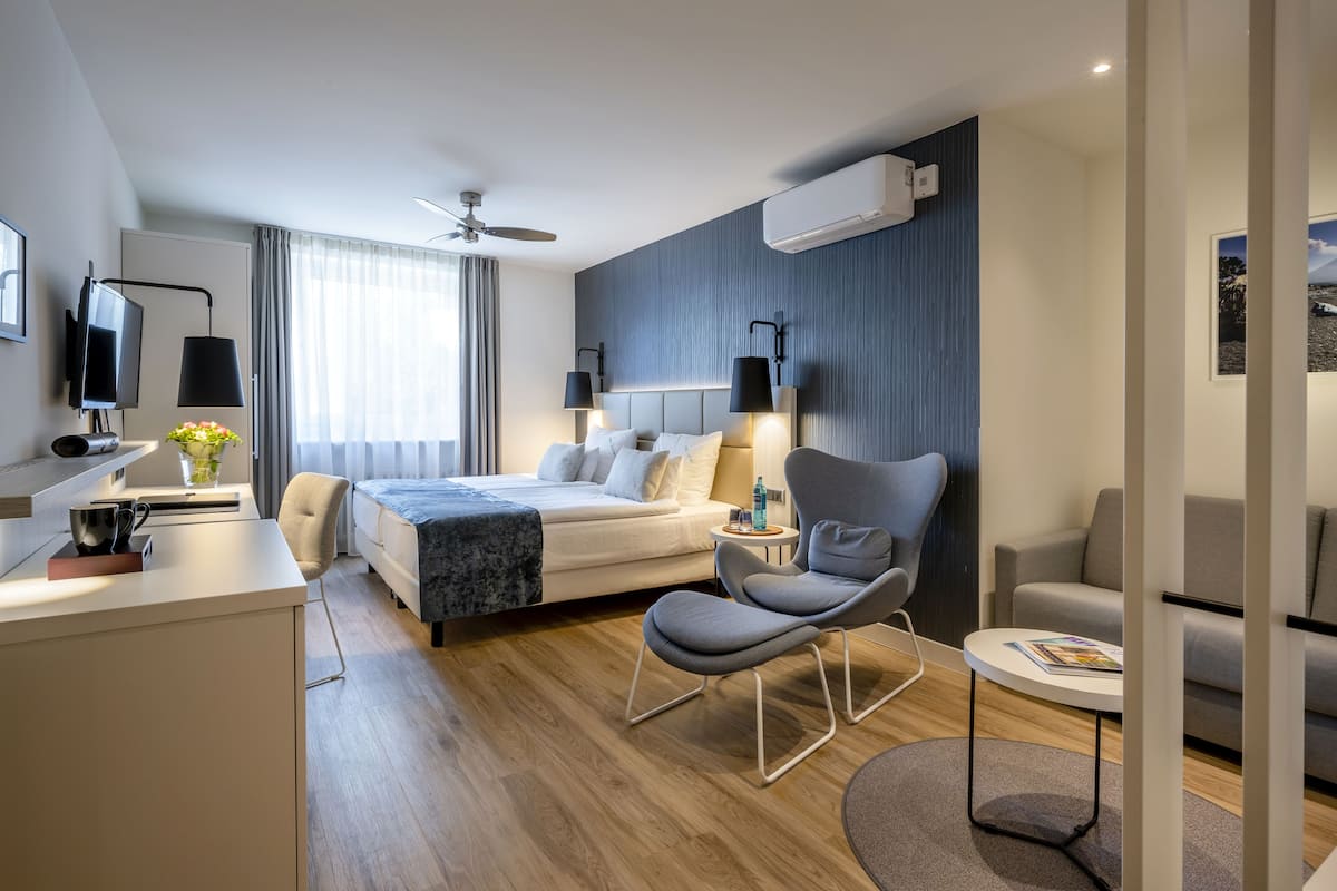 Une chambre d’hôtel moderne équipée d’un lit, de deux fauteuils, d’un bureau et d’une télévision.