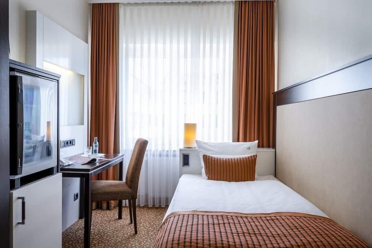 Une chambre d’hôtel avec un lit, un bureau et une chaise, une télévision et une fenêtre avec des rideaux.