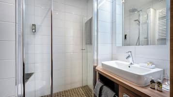 Un baño moderno con ducha envuelta en vidrio, un lavamanos blanco con tocador de madera y un espejo sobre el lavamanos.