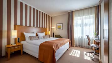 Et hotelværelse med en stor seng, et skrivebord med stol, en lampe og et vindue med gardiner.