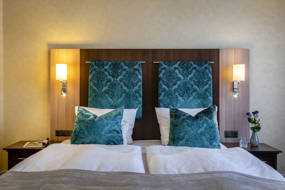 Une chambre d’hôtel avec un grand lit, deux tables de chevet, une petite table, une lampe et un vase avec des fleurs.
