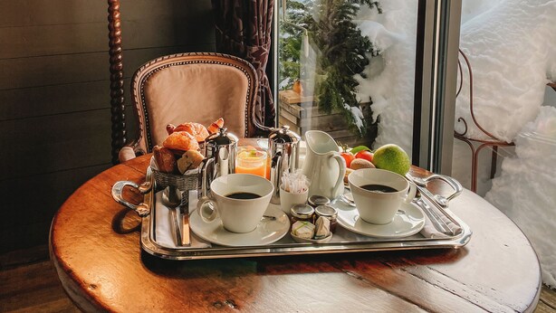 Una mesa de comedor con alimentos para el desayuno, una lámpara y vistas a casas cubiertas de nieve.