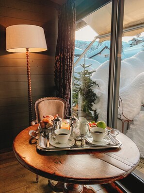 Una mesa de comedor con alimentos para el desayuno, una lámpara y vistas a casas cubiertas de nieve.