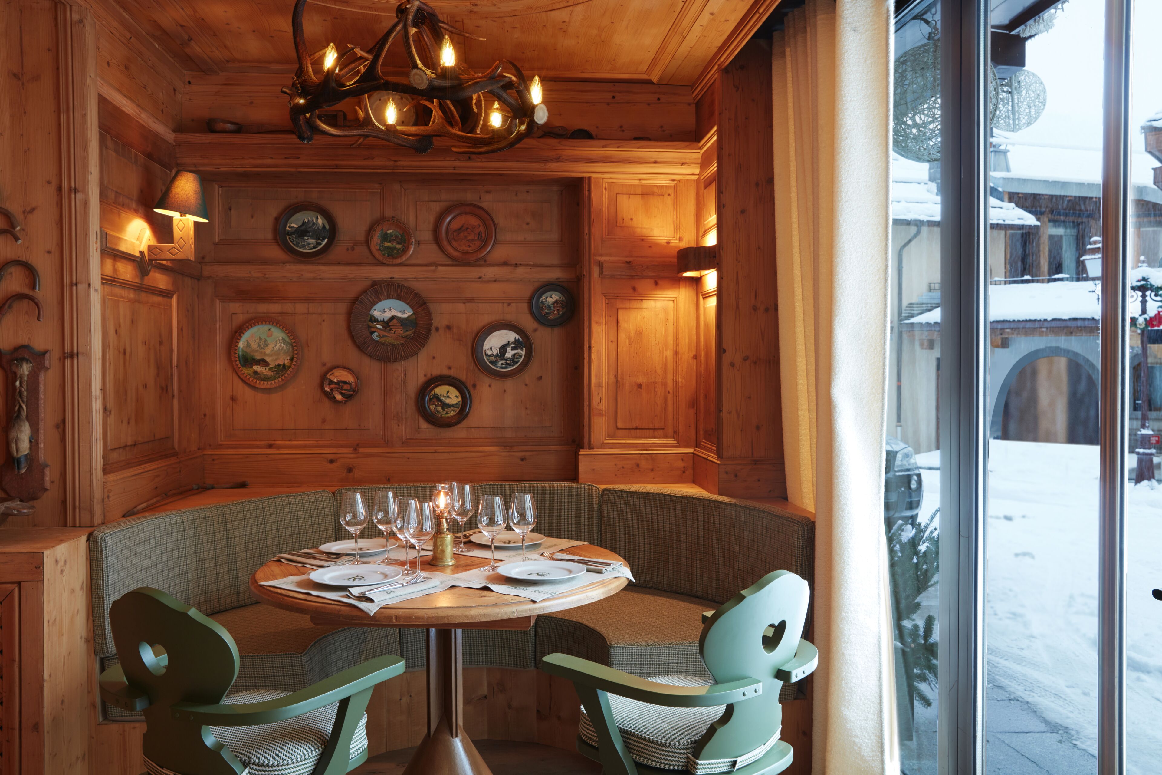 A wooden interior with a round table set for dining, surrounded by green upholstered chairs.