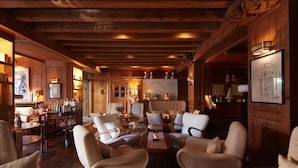 Un interior acogedor con paneles de madera, un área de estar con sillas modernas y una pequeña mesa, rodeado de vigas de madera e iluminación cálida.