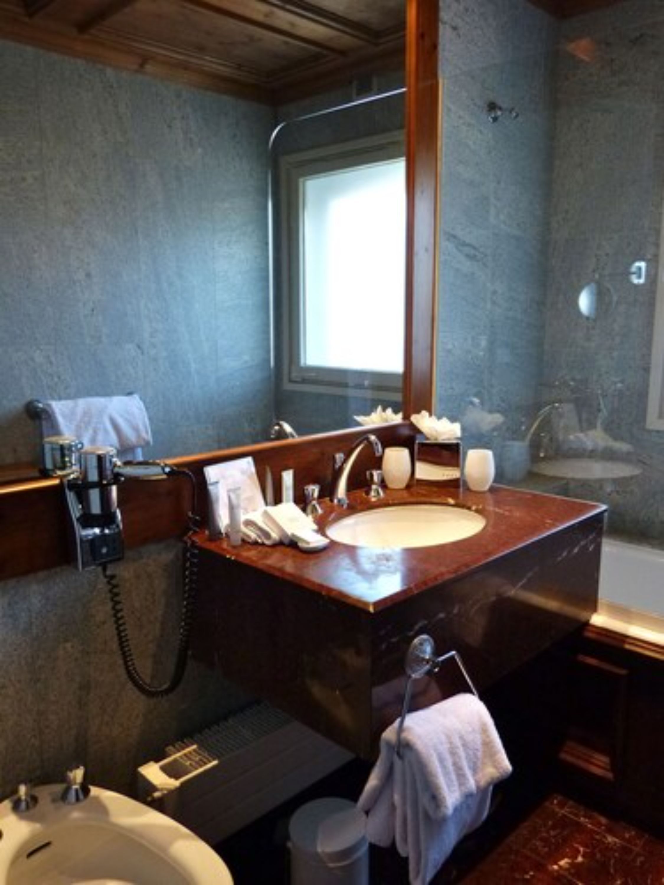 Een badkamer met een marmeren wastafel, een spiegel, een handdoekhouder en een douche.