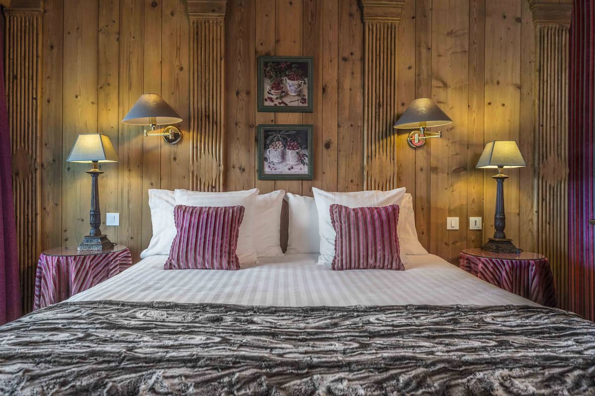 A bed with a striped pillow set, two wall-mounted lamps, and two framed pictures on the wall.