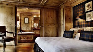 Una habitación de madera con una cama, una silla, una tocador con espejo y una pared decorada con cuadros.