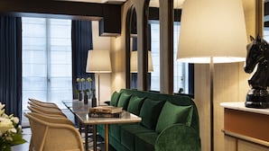 Una habitación de hotel moderna con un sofá verde, una mesa de comedor con sillas y una lámpara grande.