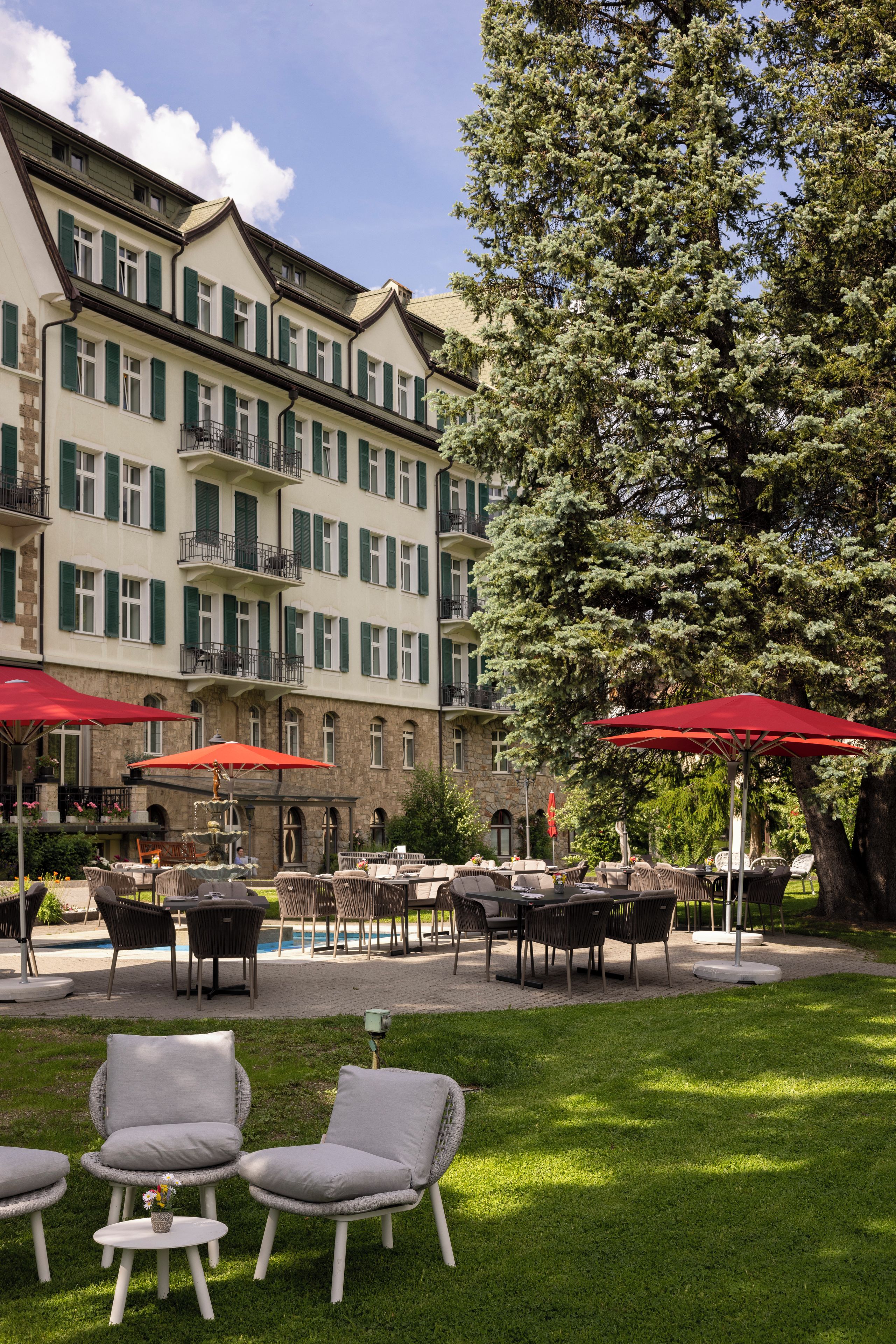 Un patio de hotel con mobiliario exterior, una piscina y un árbol grande.