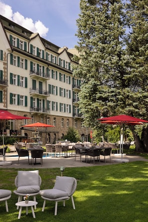 Un patio de hotel con mobiliario exterior, una piscina y un árbol grande.