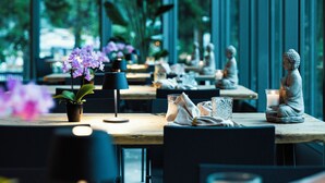 A modern dining area with large windows, potted plants, and a Buddha statue. - Cresta Palace (Celerina-Schlarigna)