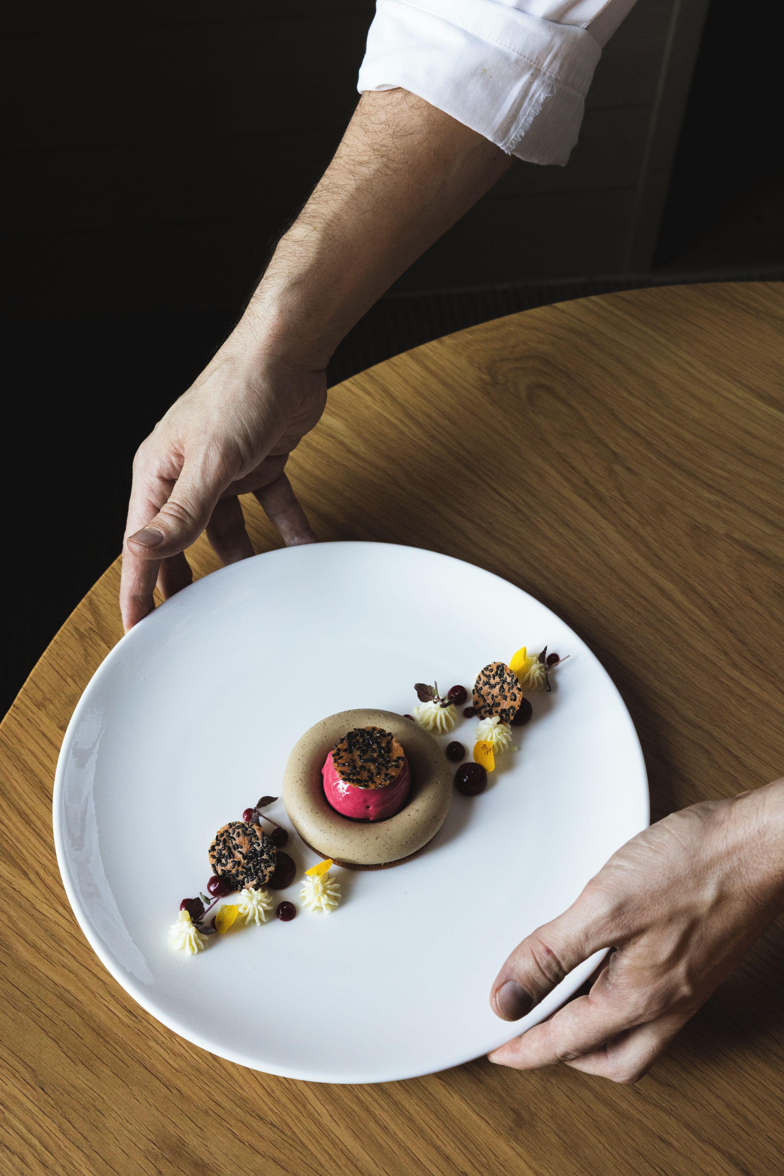 A person holding a white plate with a dessert on a wooden table.