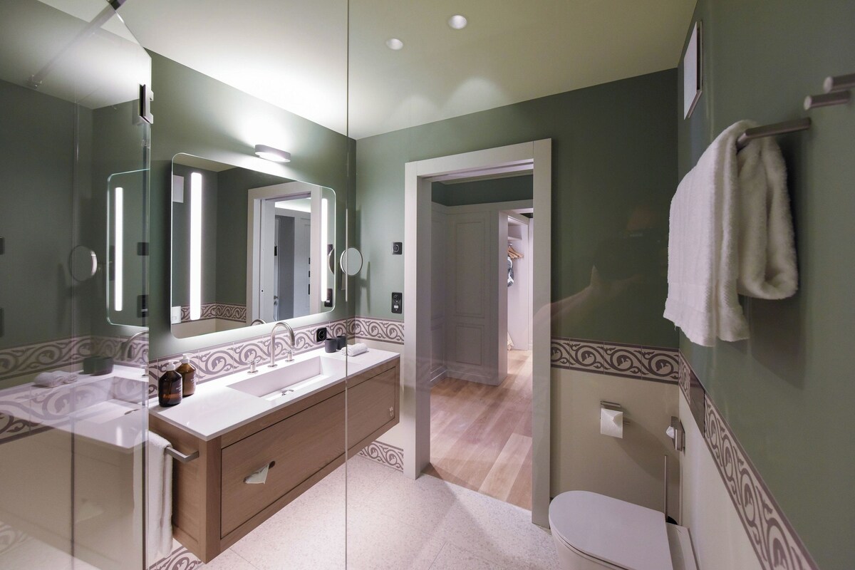 A modern bathroom with a large mirror, a sink, and a toilet.