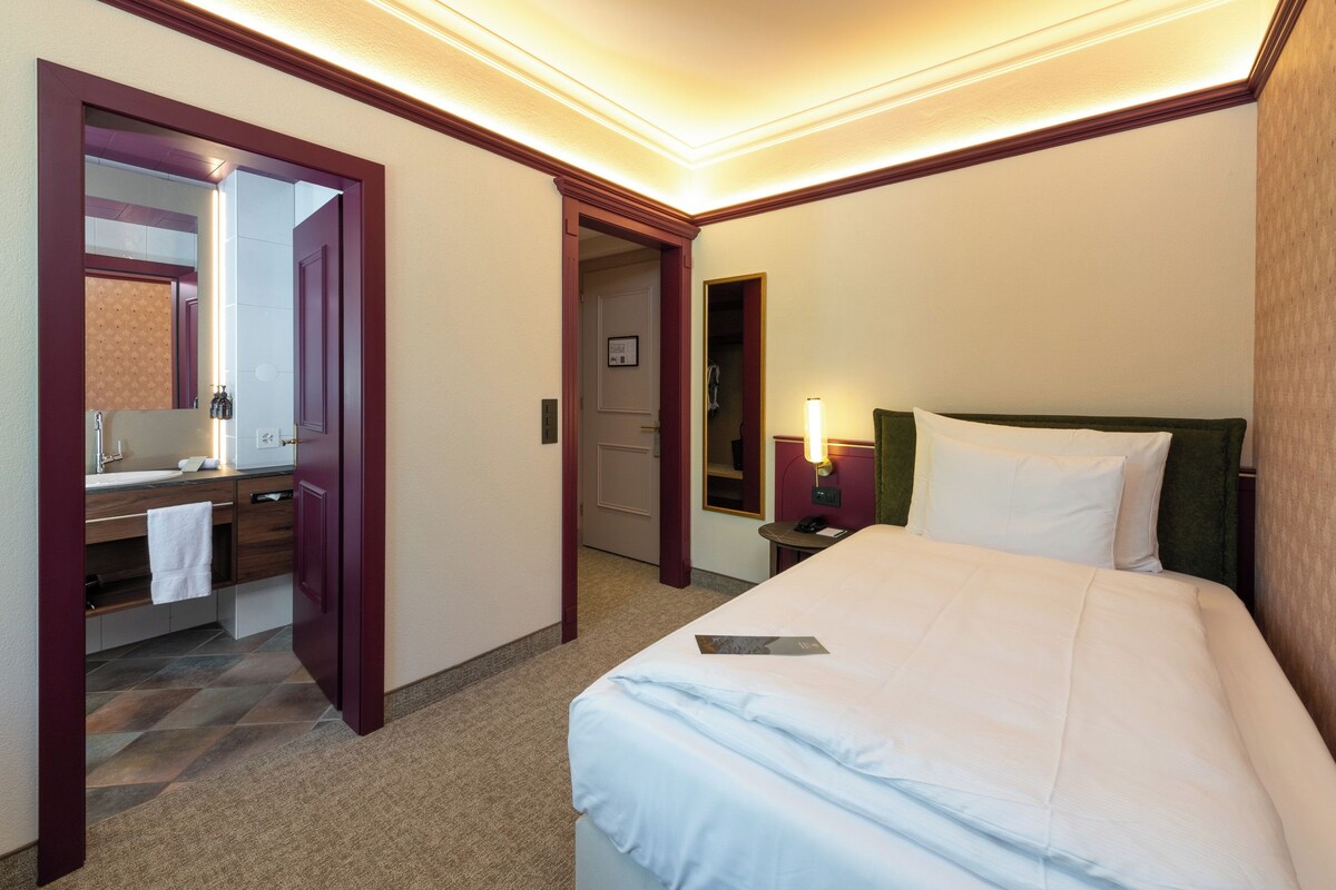 Quarto de hotel com cama, banheiro com espelho, pia e toalha.