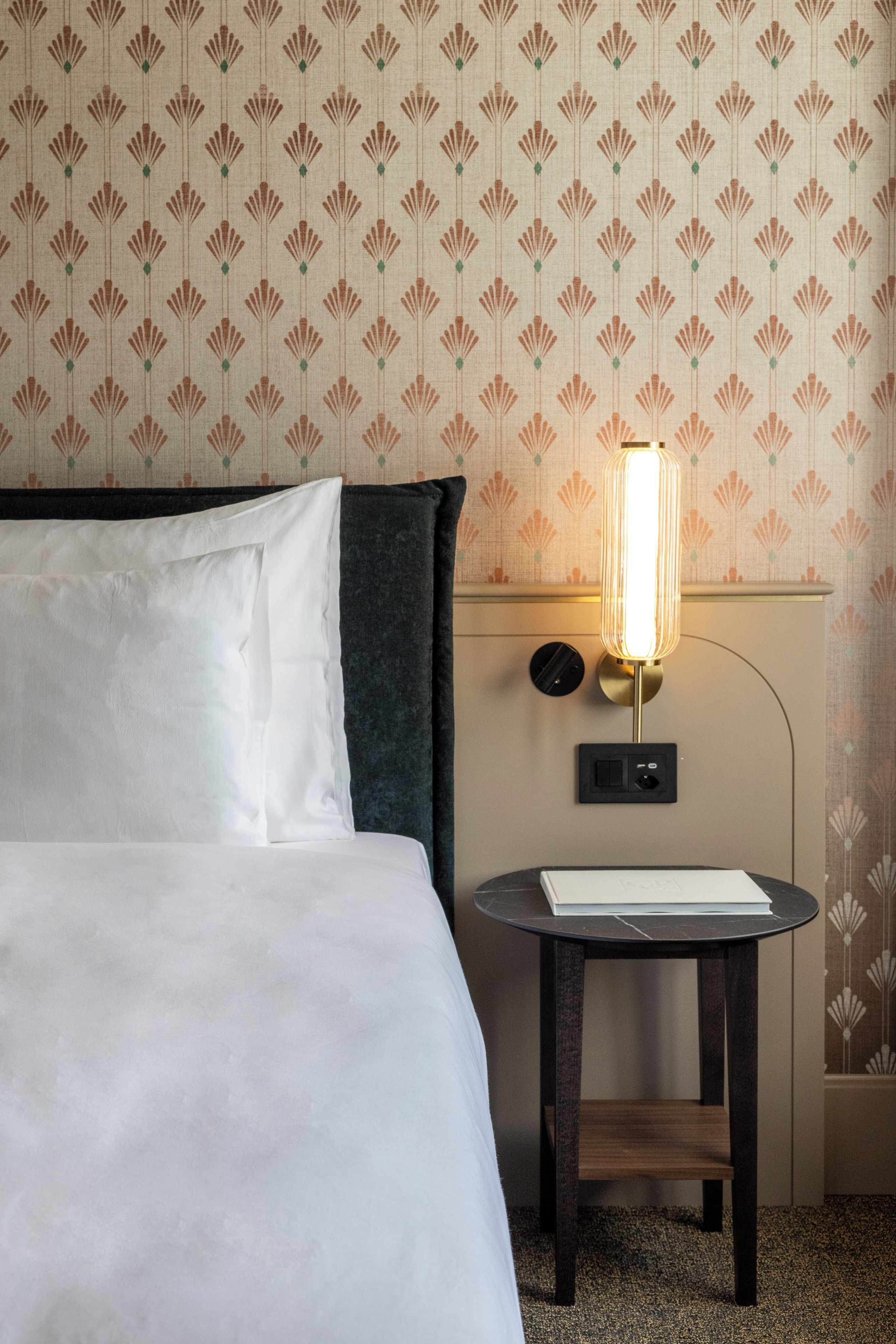 Una habitación de hotel con una cama, una mesita de noche con una lámpara y una pared con estampado de flores.