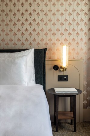 Una habitación de hotel con una cama, una mesita de noche con una lámpara y una pared con estampado de flores.