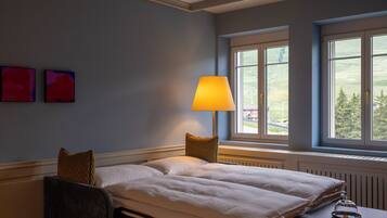 A bedroom with a bed, a bedside table with a lamp, and a window with a view of the outdoors.