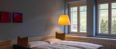 Un dormitorio con una cama, una mesita de noche con lámpara y una ventana con vistas al exterior.