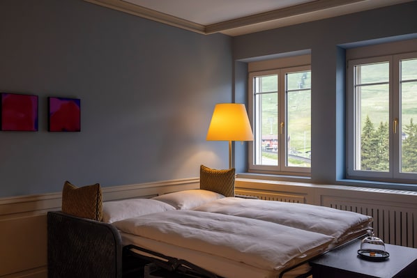 Un dormitorio con una cama, una mesita de noche con lámpara y una ventana con vistas al exterior.