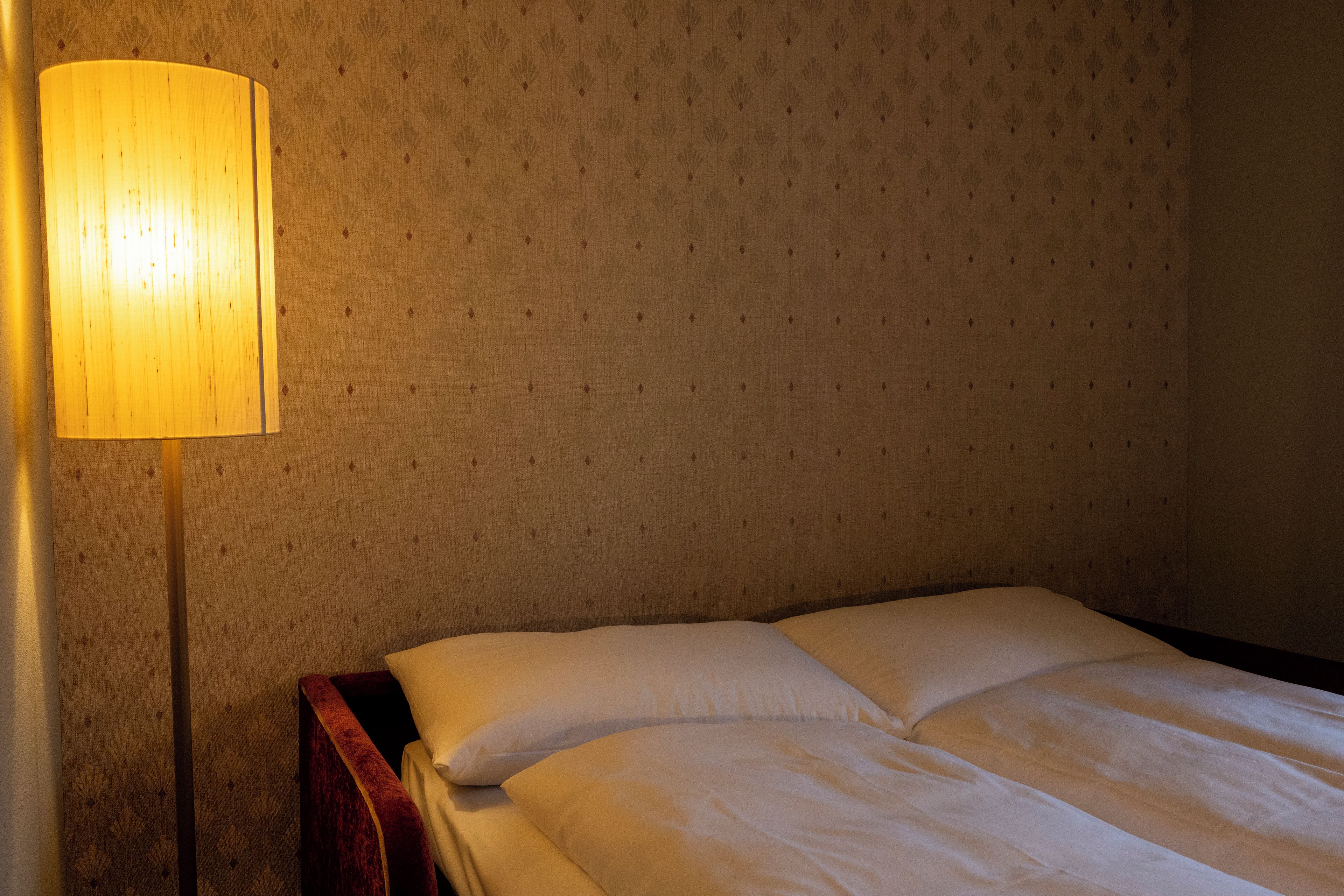 A hotel room with a bed, pillows, and a standing lamp.