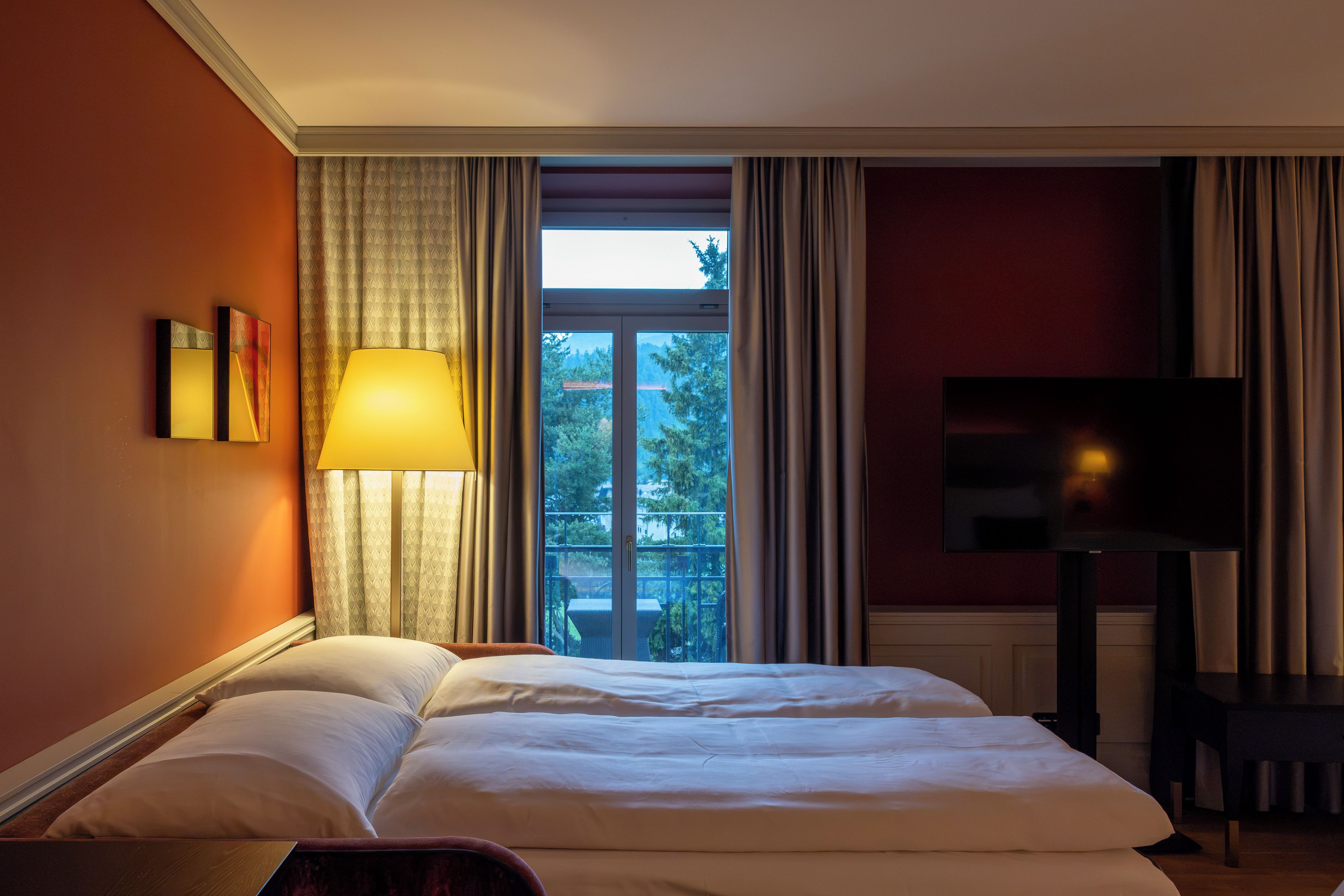 Een hotelkamer met een bed, een televisie, een lamp en een raam met gordijnen.