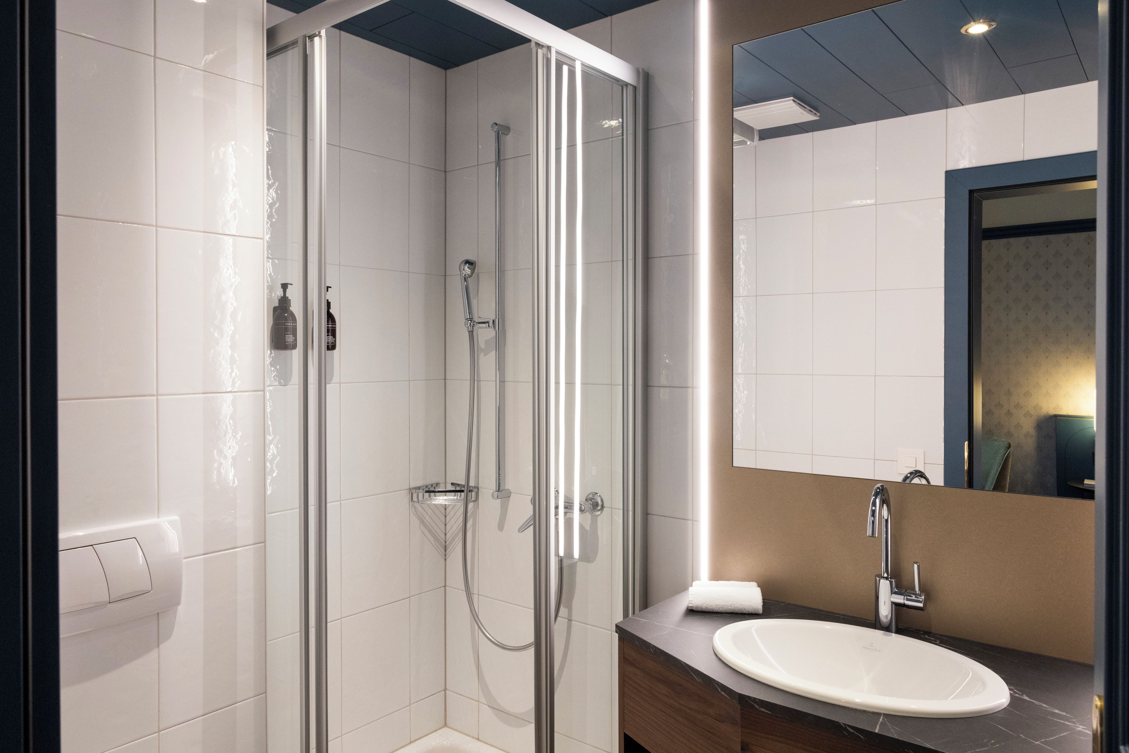 Un baño moderno con cabina de ducha acristalada, un lavabo blanco y un espejo con marco oscuro.