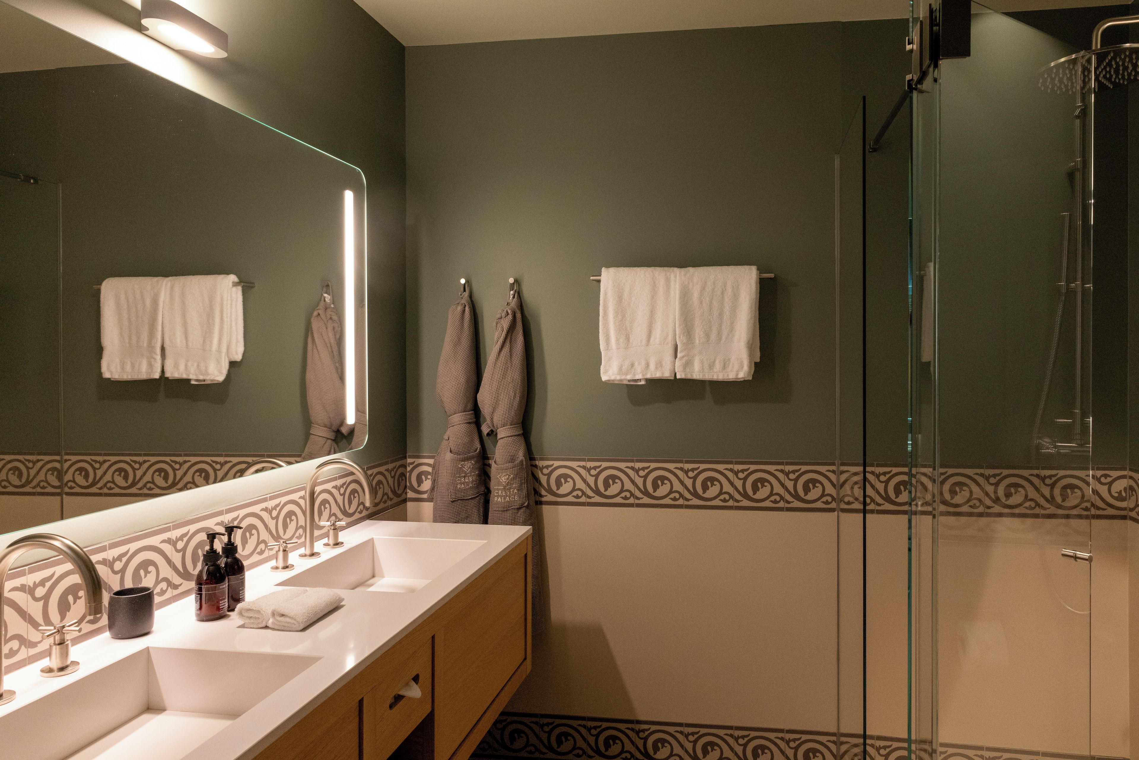 A bathroom with a double sink vanity, a glass shower enclosure, and decorative wall tiles.