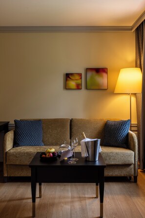 Habitación de hotel con sofá, una mesa con frutero, copas de vino y una botella de champán.