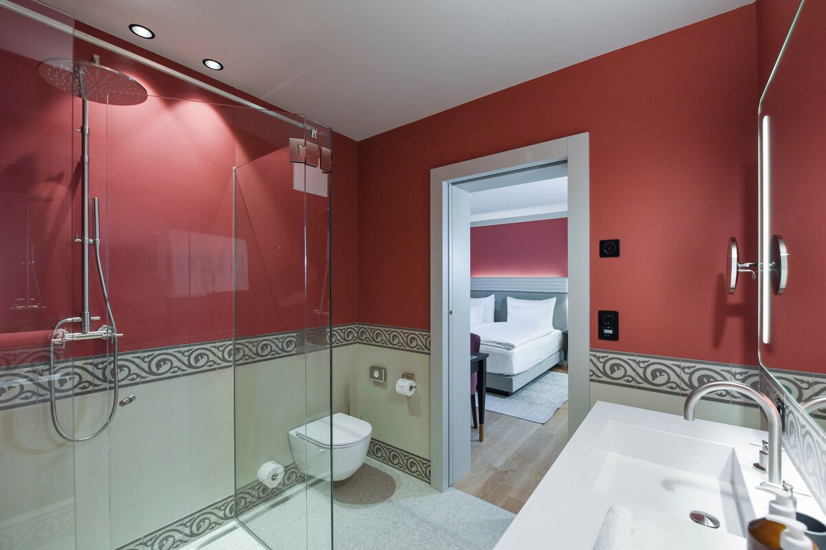 Un baño moderno con ducha de vidrio, lavamanos blanco y un inodoro a la vista.