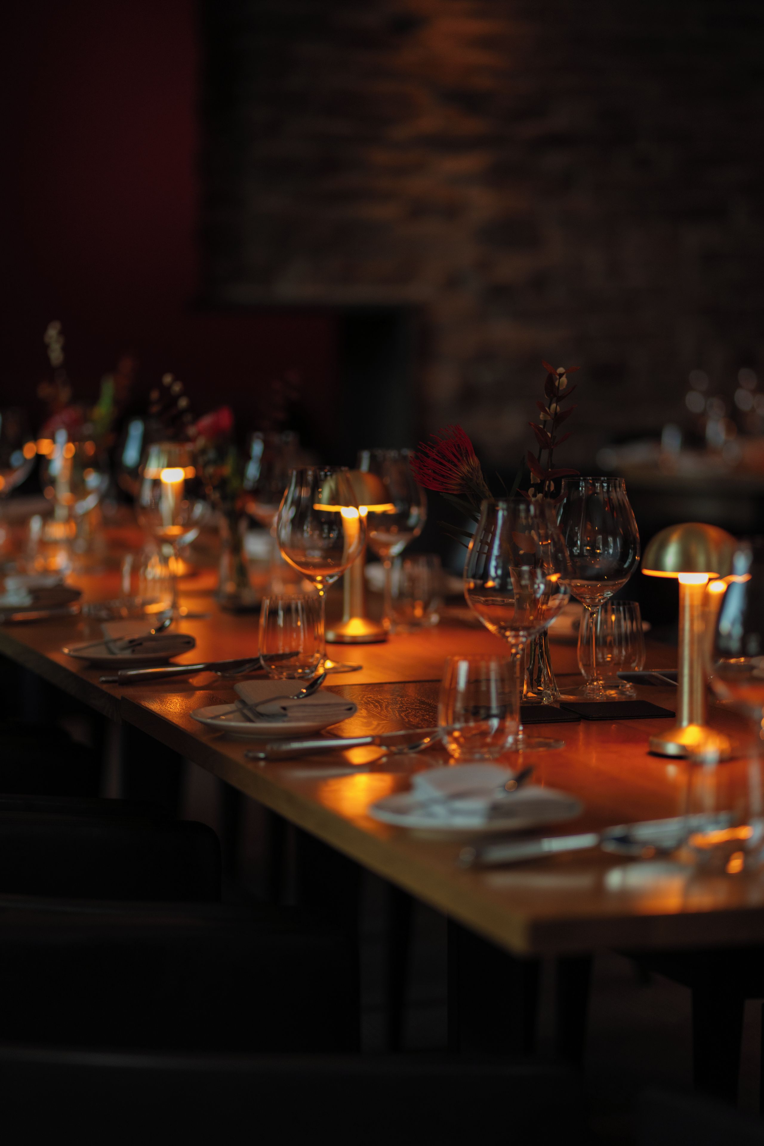 Ein schwach beleuchteter Restauranttisch, gedeckt mit Weingläsern, Tellern und Besteck.