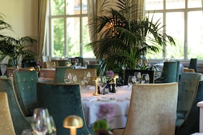 Un comedor con mesas redondas, sillas y una planta grande en maceta.
