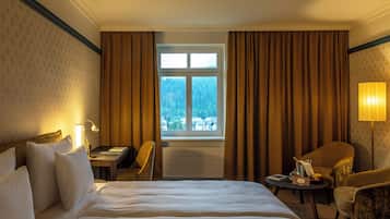 Habitación de hotel con cama, escritorio, silla, lámpara y vista a un bosque por la ventana.