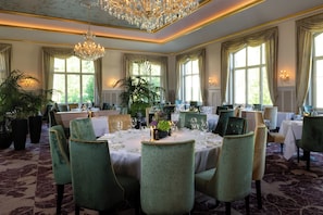 A formal dining room with a chandelier, large windows, and green upholstered chairs.