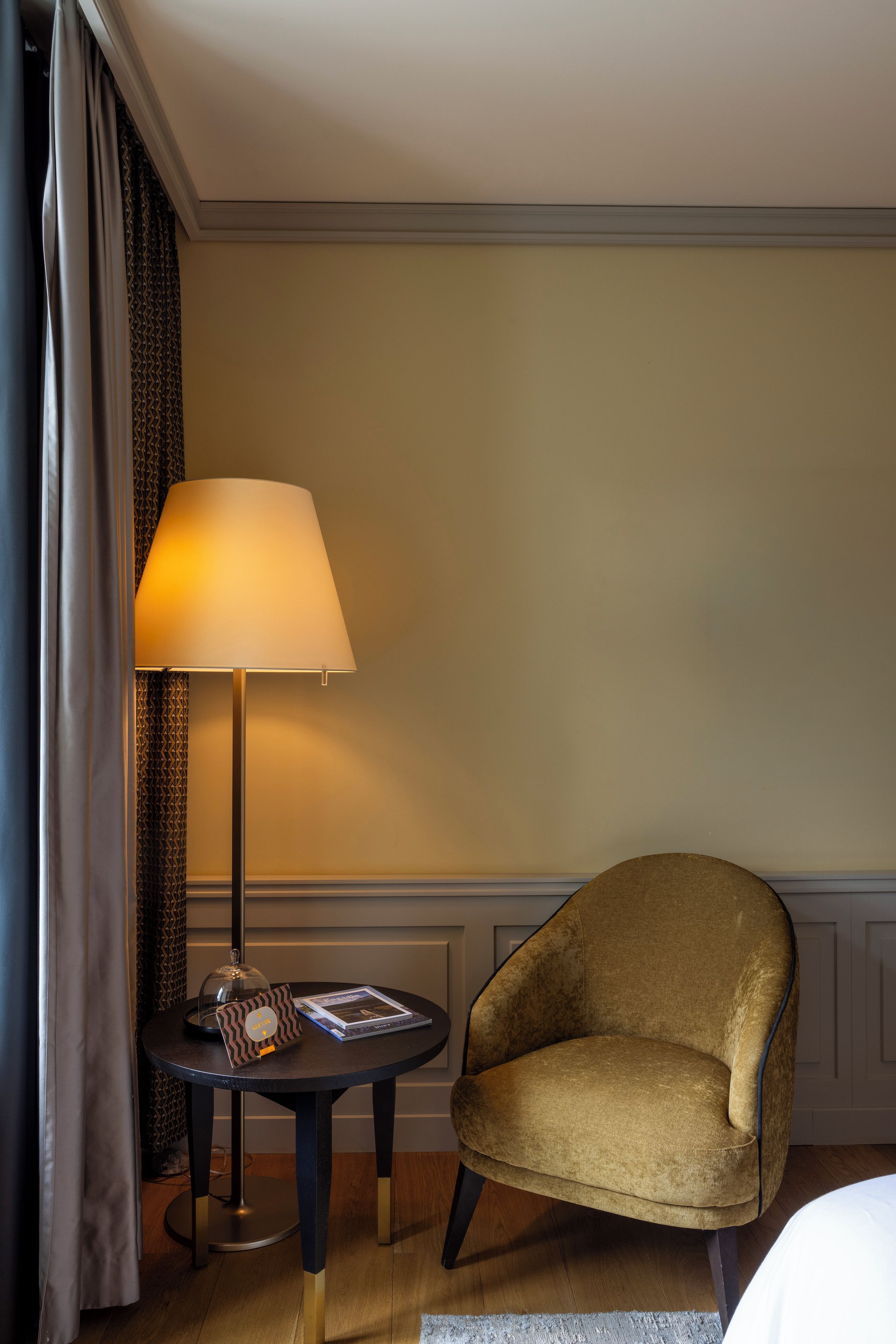 Hotellihuone, jossa on pyöreä pöytä, lamppu, tuoli ja sänky.