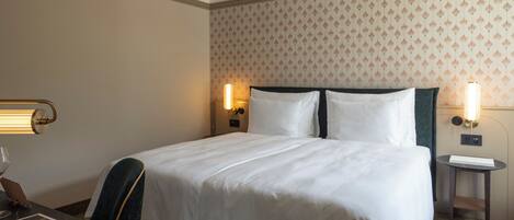 A hotel room with a large bed, two bedside lamps, a small table, and a chair.